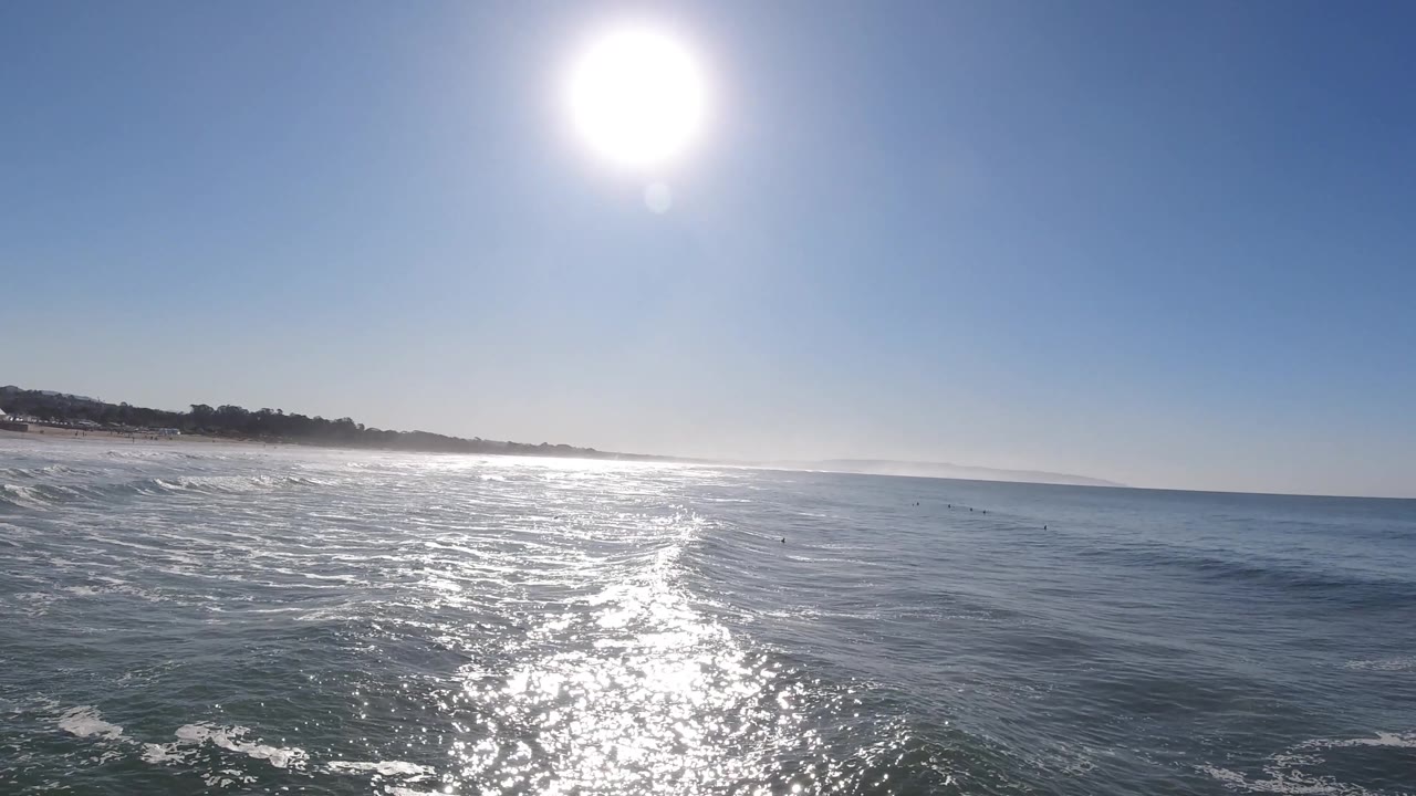 Open ocean fills the foreground while the sun reflection angles across the water toward a low Pismo Beach shoreline, with no clearly visible people.
