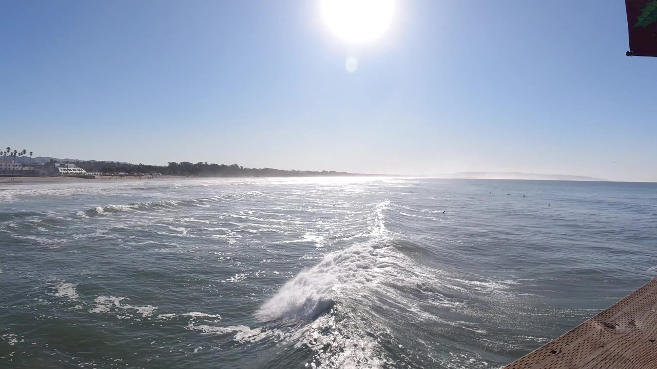 Breaking wave and reflective water with shoreline buildings in the background.