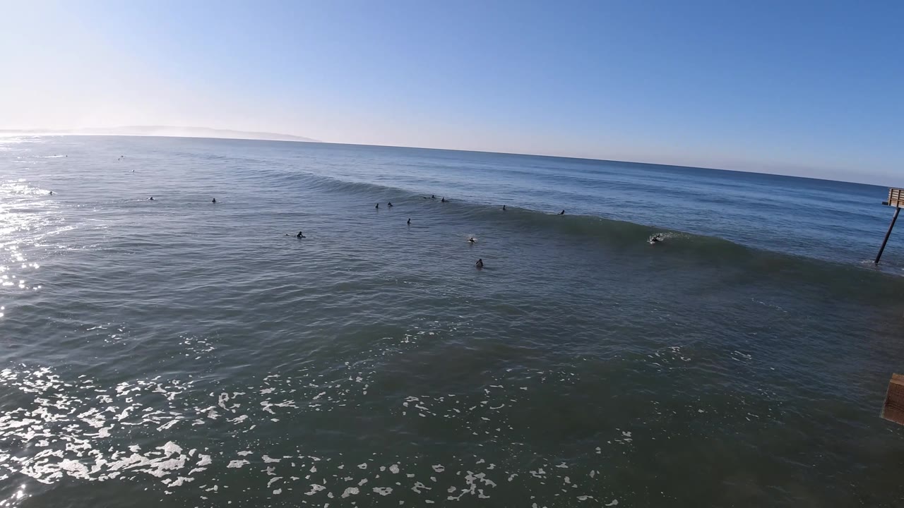 Wide surf lineup with a pier edge entering from the right.