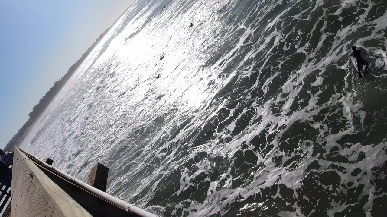 Foamy ocean surface with surfers beside a wooden deck corner.