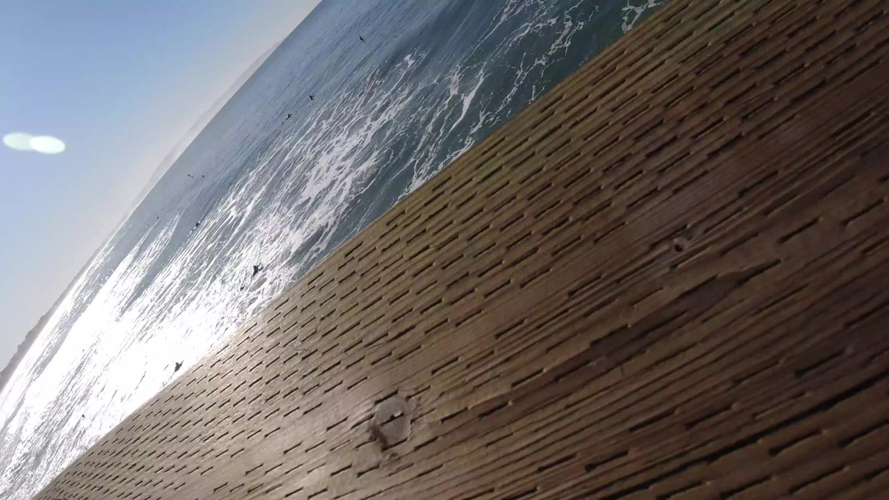 A second Pismo Beach frame repeats the diagonal ocean view, with foamy water beside the timber boardwalk and no visible people.