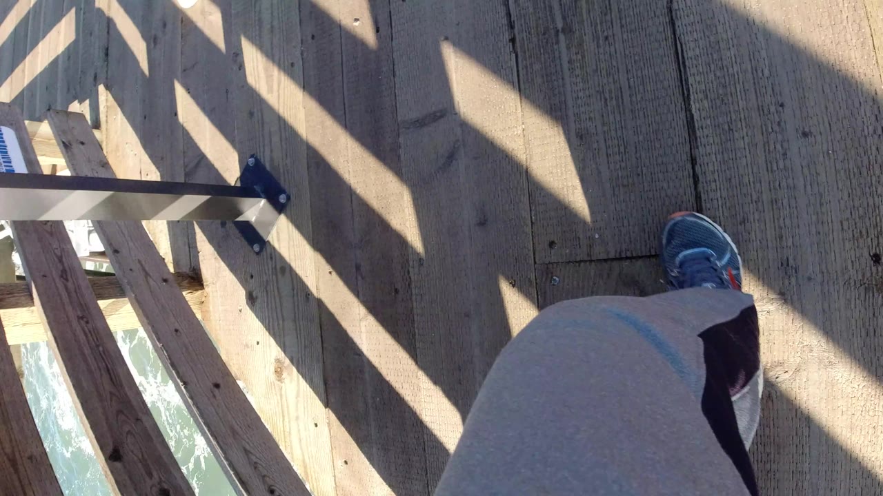 Two walkers' legs and shoes on a wooden boardwalk.