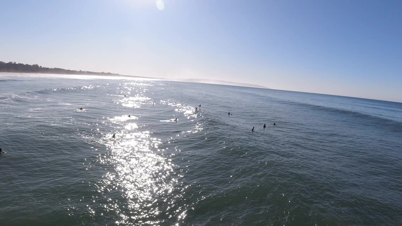 Sun glare on ocean water with scattered surfers or swimmers.