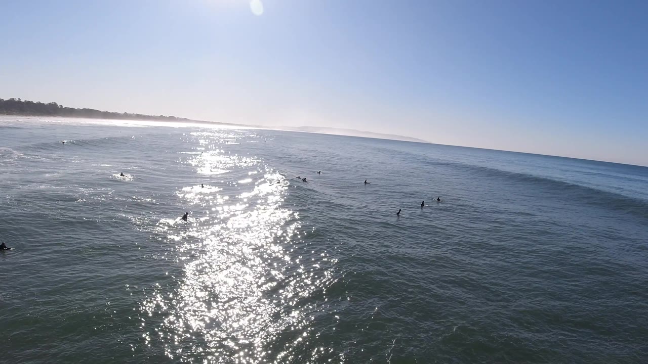 At Pismo Beach, several small figures are visible in the ocean while a low swell begins to break through the sunlit water path.