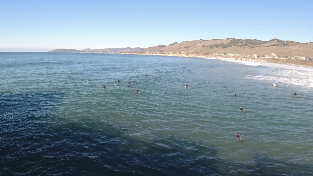 Elevated view of ocean swimmers with a beach and hills behind them.