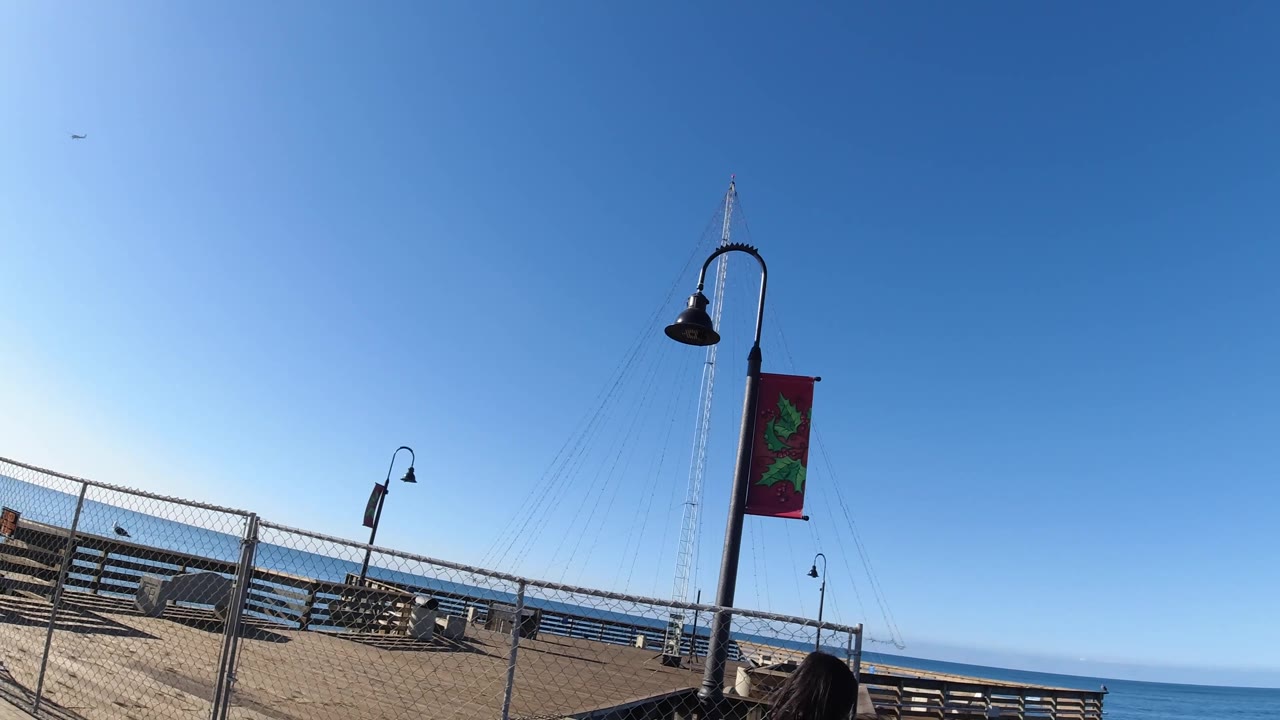 Slanted boardwalk with lamps, fence, benches, ocean, and partial head at bottom edge.