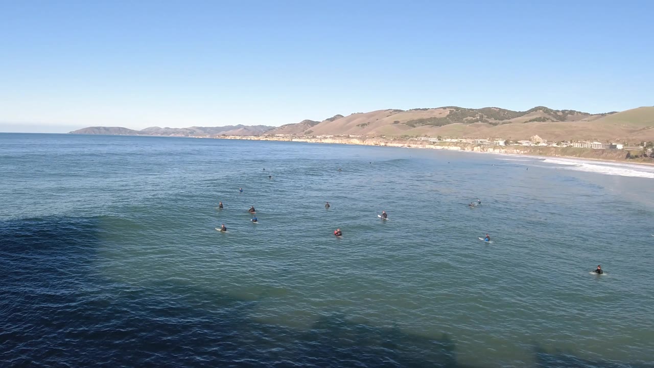 Calm ocean surface with several bathers and a sandy beach along the right side.