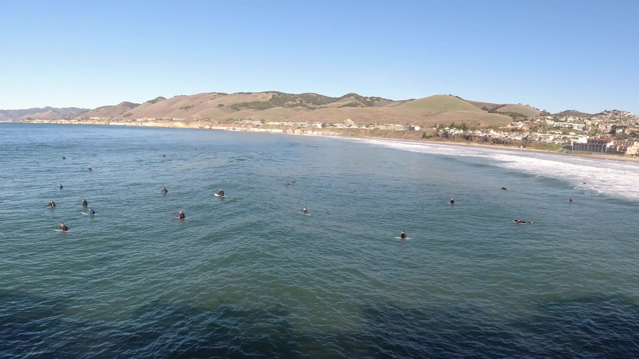 Drone view of nearshore water with people spread across the surface and beach behind.