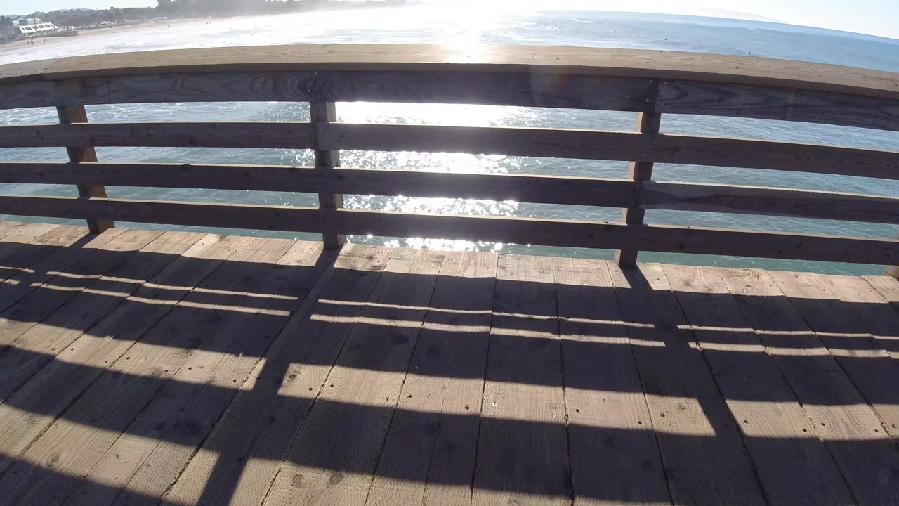Wooden railing over blue water with bright reflection and beach.
