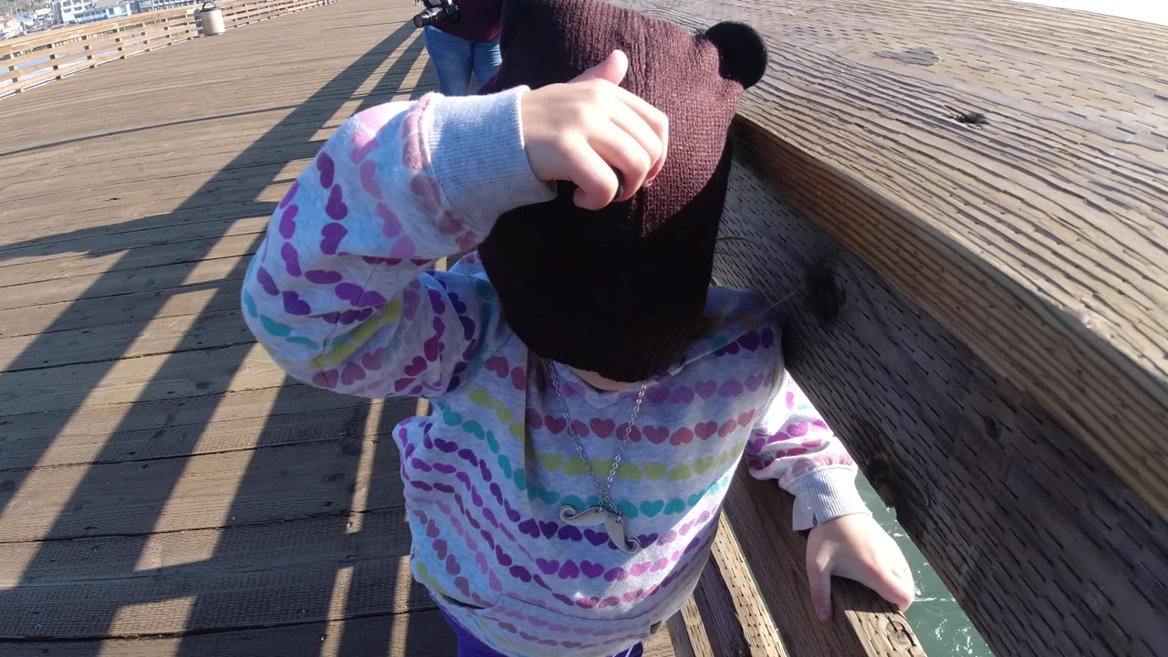 Closer view of child touching a dark knit cap on the pier.