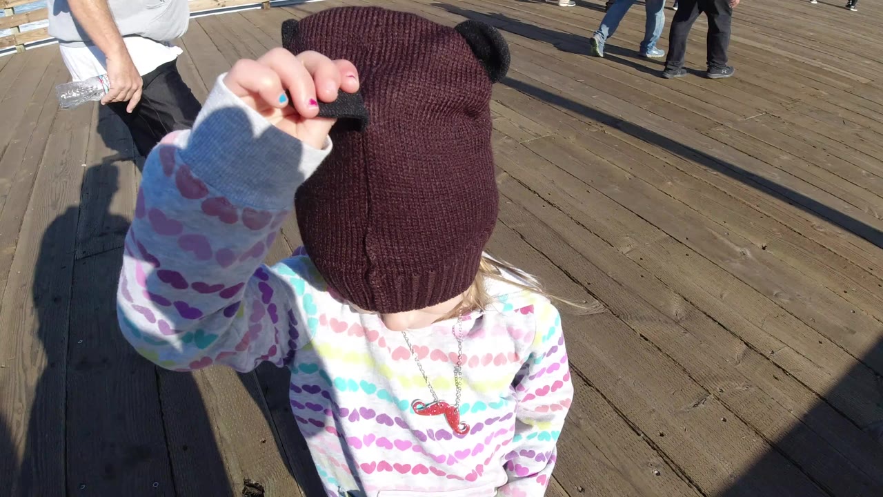 Child raises a hand near a dark beanie on the dock.