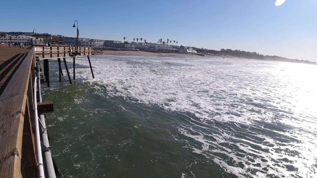 Pier railings and lamp posts overlook a broad field of white surf.