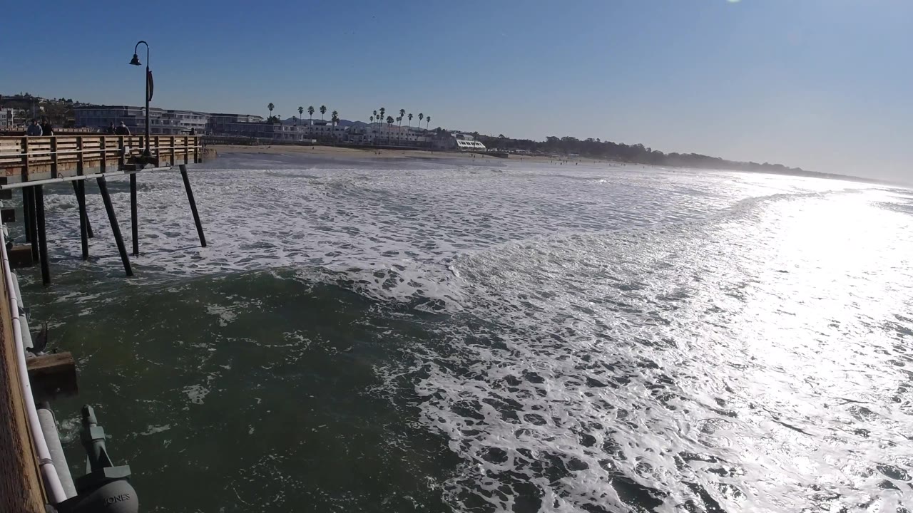 Pier corner and foamy ocean with a bright reflection path across the water.