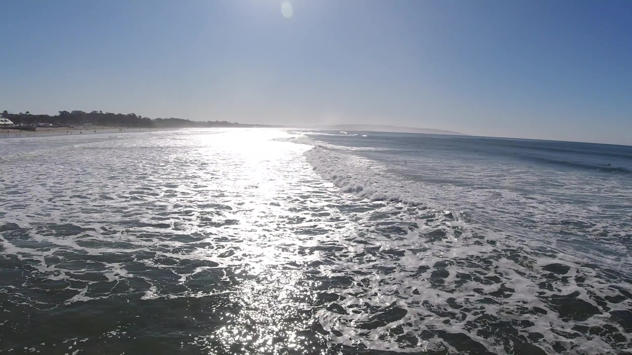 Foamy waves spread across the ocean with a hazy shoreline behind.