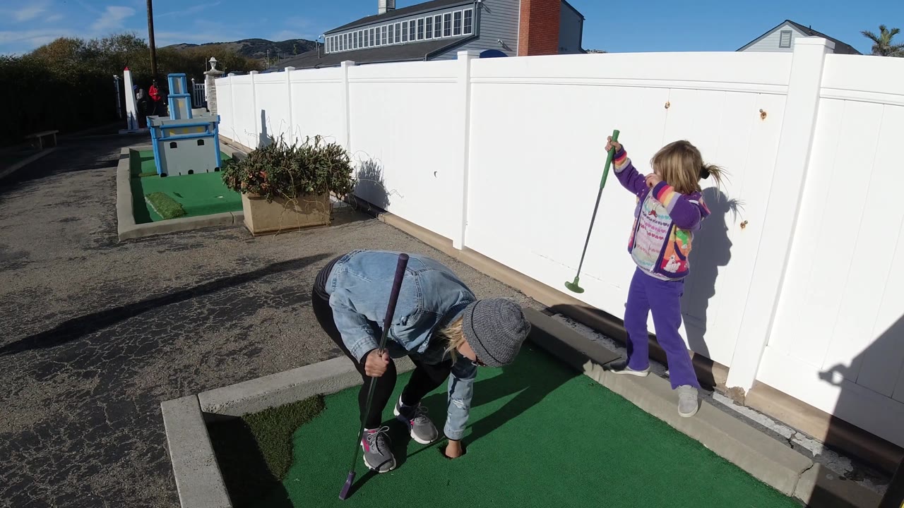 Woman bends down near the mini-golf hole while the child raises a club.