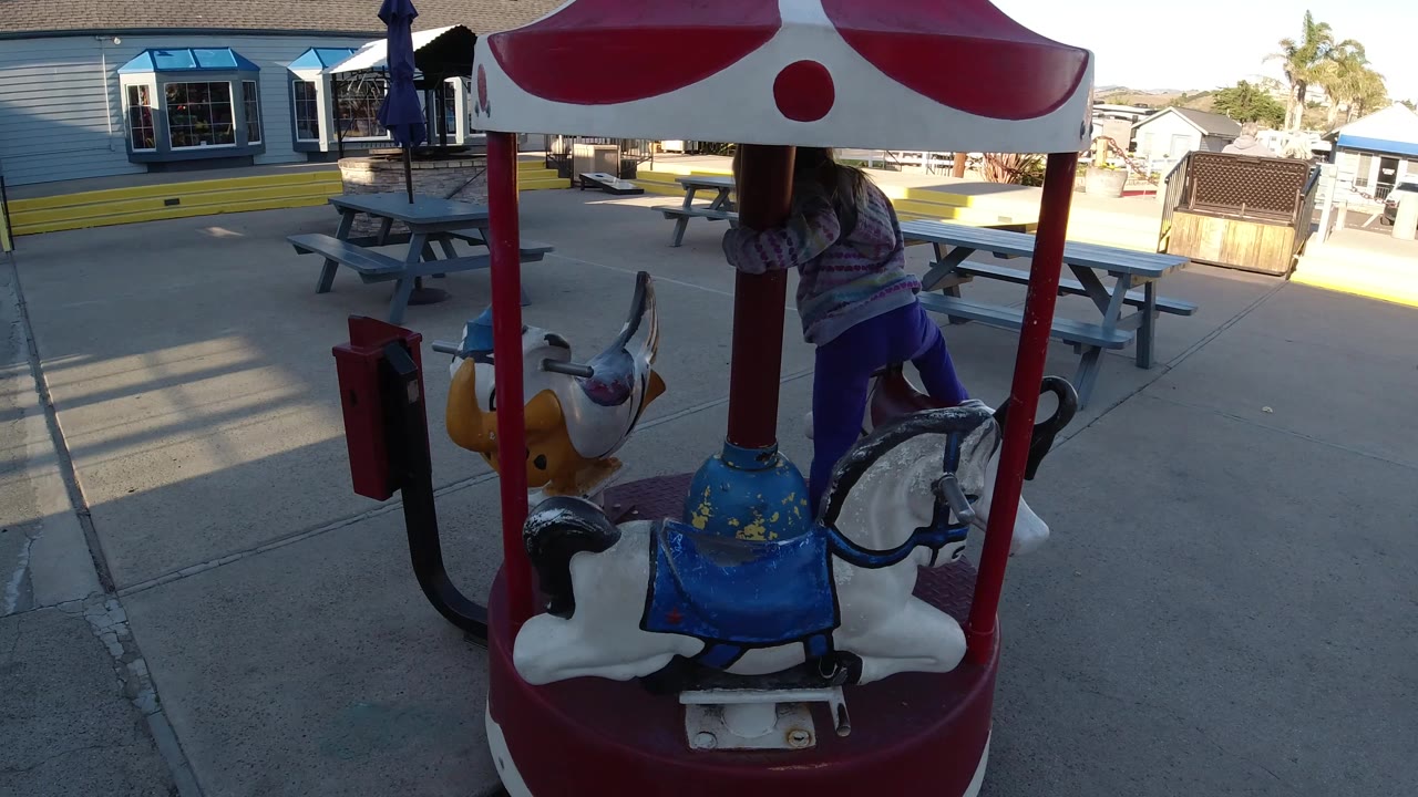 Young girl moves behind the center pole of a small carousel ride.