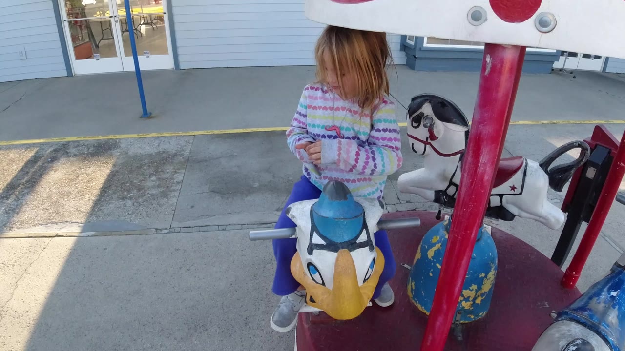 Child sitting on a merry-go-round animal with a horse figure behind her.