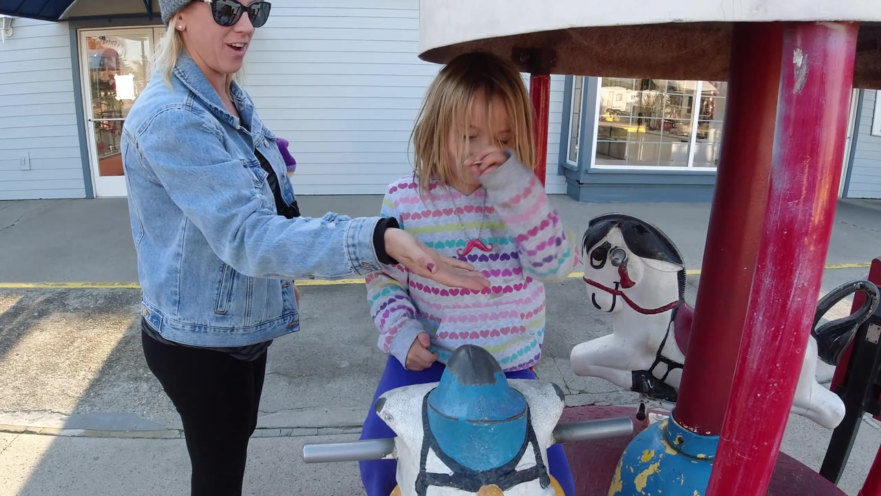 Woman reaches toward girl seated on carousel horse.