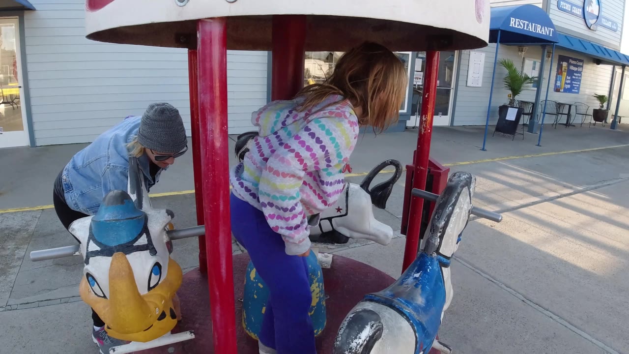 Girl on the carousel with an adult bent near a yellow ride animal.