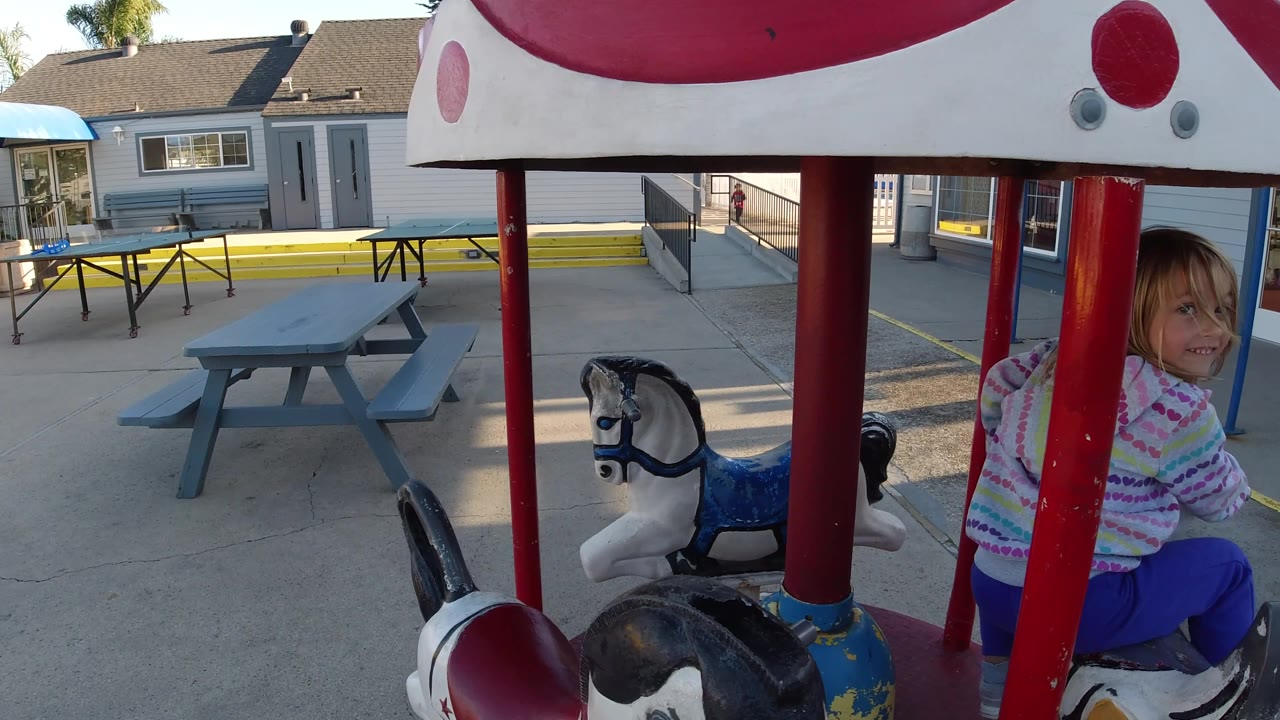 Child seated on a painted horse beside red ride supports.