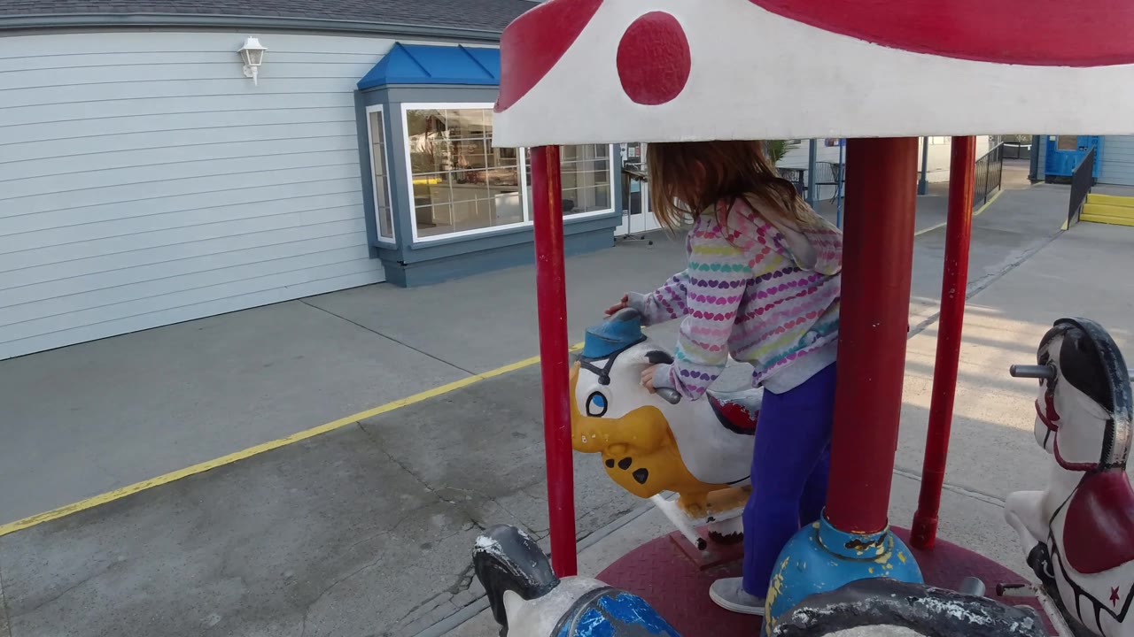 Girl holding a yellow carousel animal with storefront windows behind.