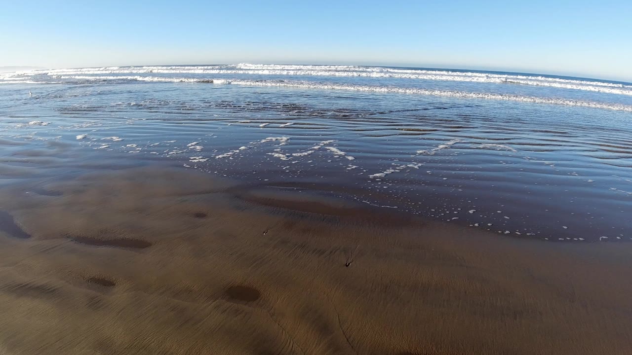 Pismo Beach shallows reflect the sky while darker ripples in the wet sand lead toward layered white surf, with no visible people.