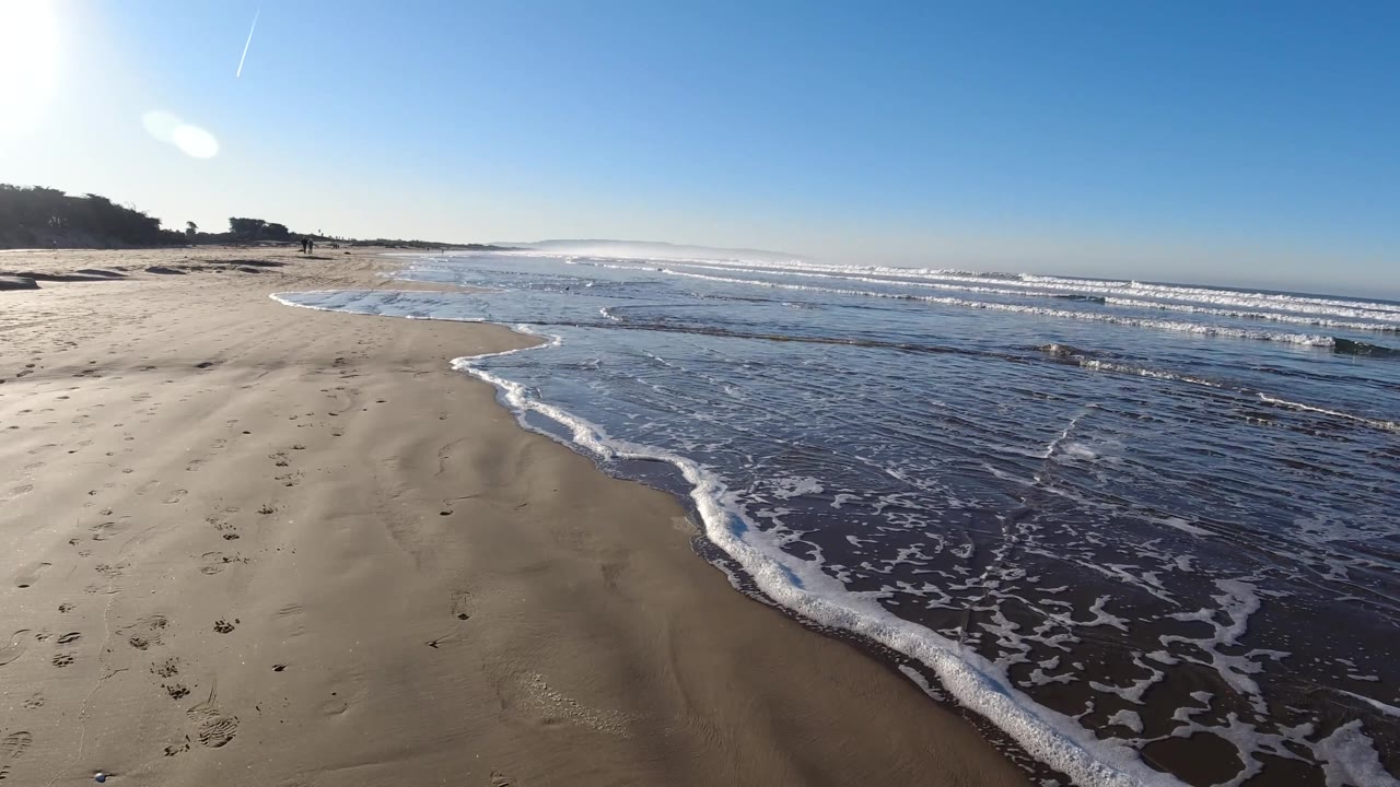 Beach surf line with wet sand, footprints, and distant walkers.