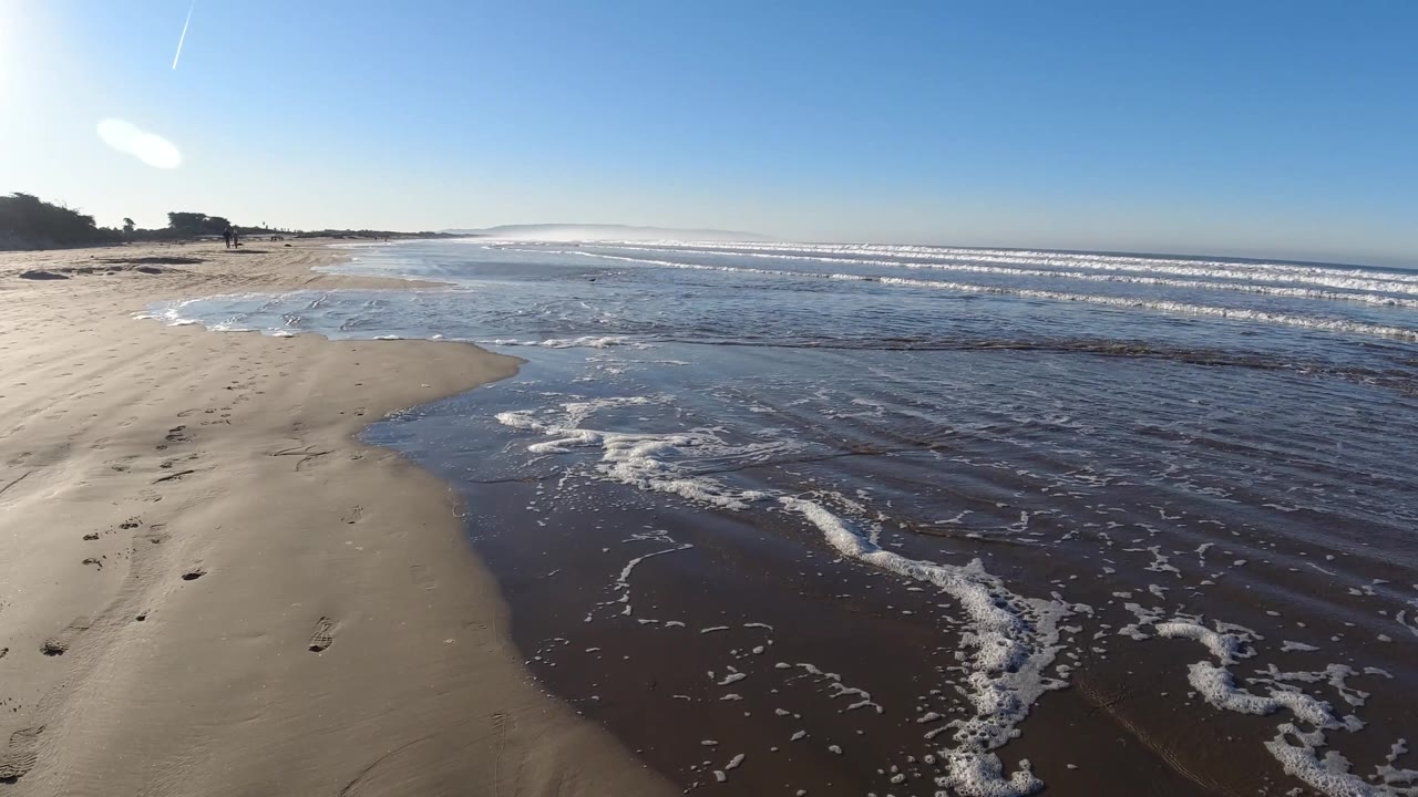 A curving edge of Pismo Beach sand borders rippled shallow water and white surf bands, with no visible people in this frame.