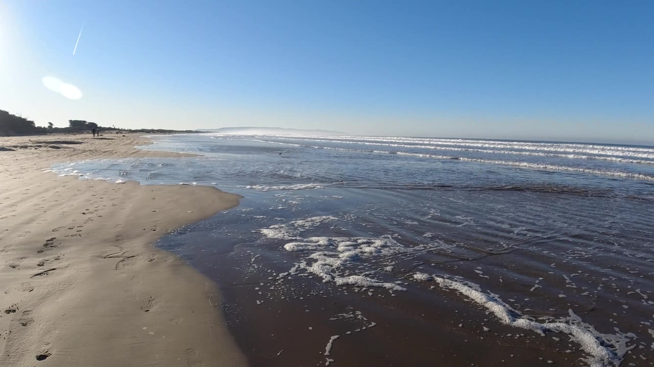 The wide Pismo Beach view holds wet sand at left, foamy water across the center, and low surf lines at right, with no visible people.