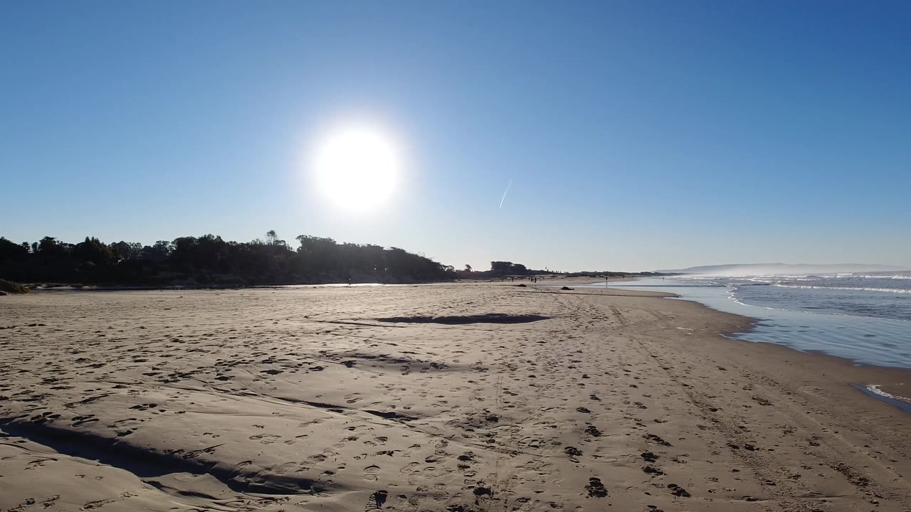 A wide Pismo Beach view shows open sand leading toward the surf, with the sun above the left side of the beach and no visible people in the frame.