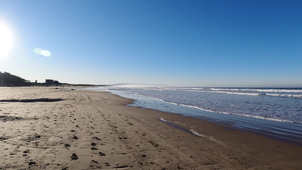 Pismo Beach view with the ocean occupying more of the right side, small white wave lines near shore, open sand to the left, and no visible people.