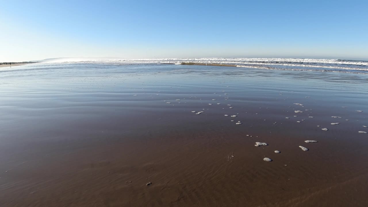 Wide wet shoreline with rippled water and distant breakers.