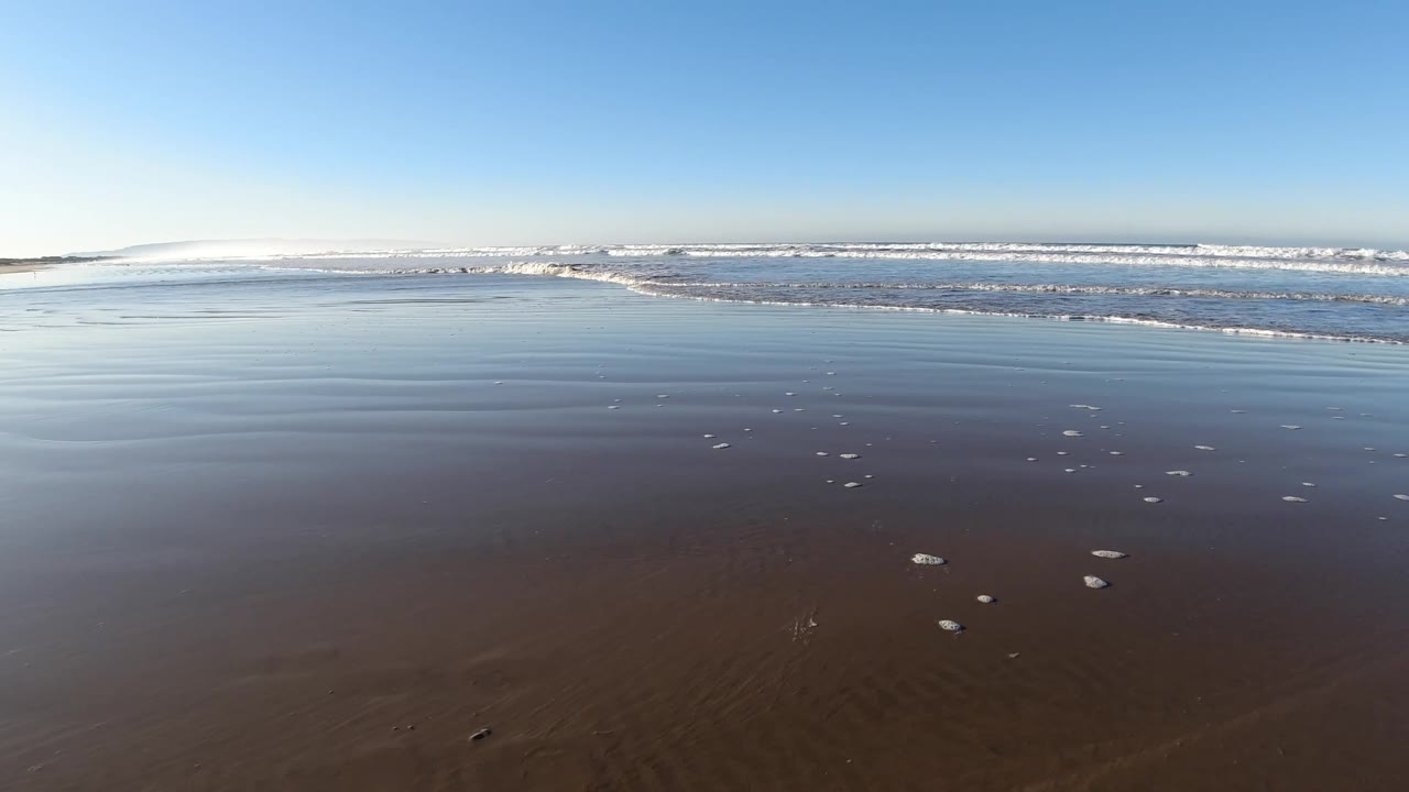 At 0:02, the Pismo Beach surf line sits high in frame while scattered white foam rests on the reflective wet sand, with no visible people.