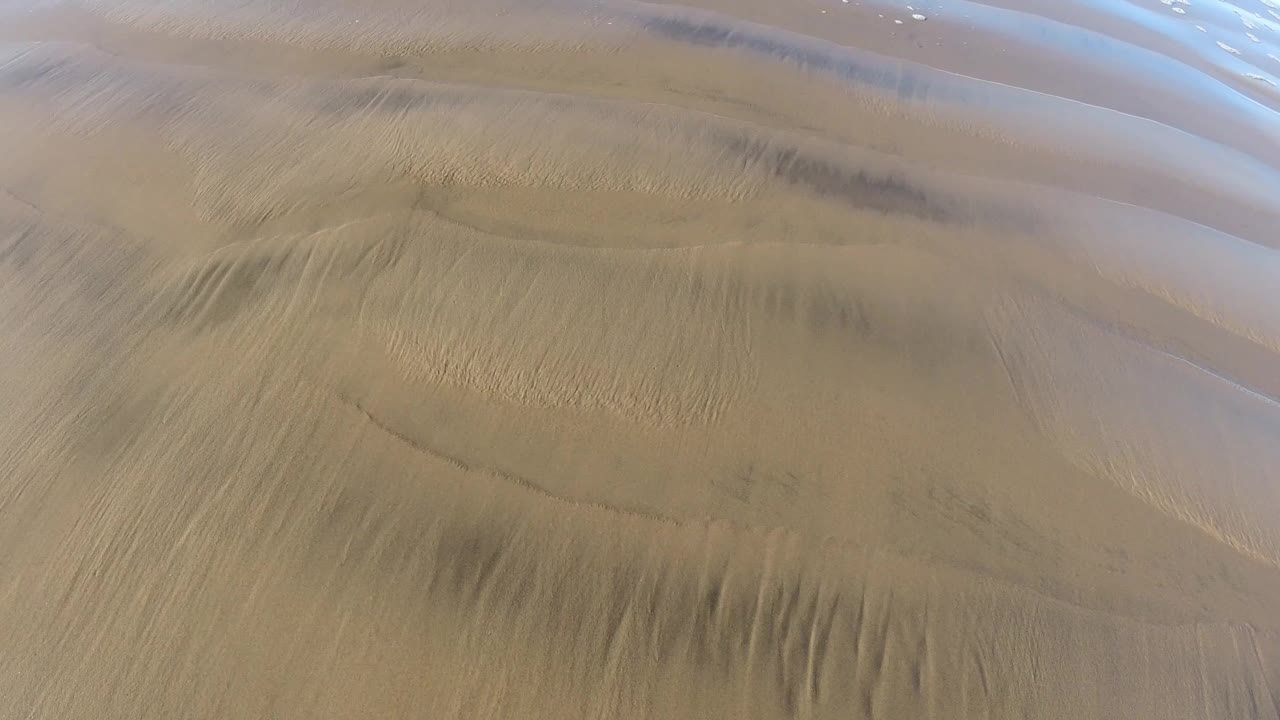 Wet rippled sand at Pismo Beach fills the frame, with thin bands of shallow water near the top and no visible people.