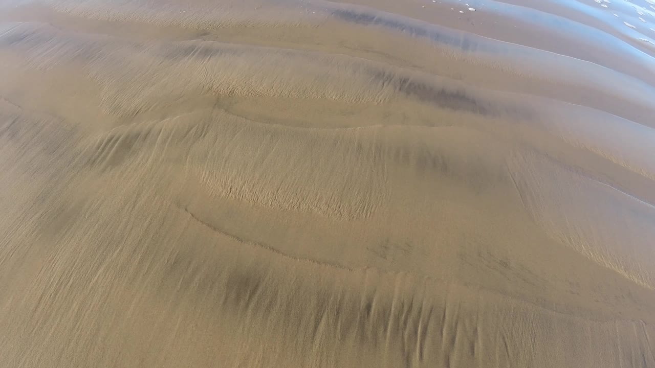 Rippled wet sand with darker streaks and a pale water band.