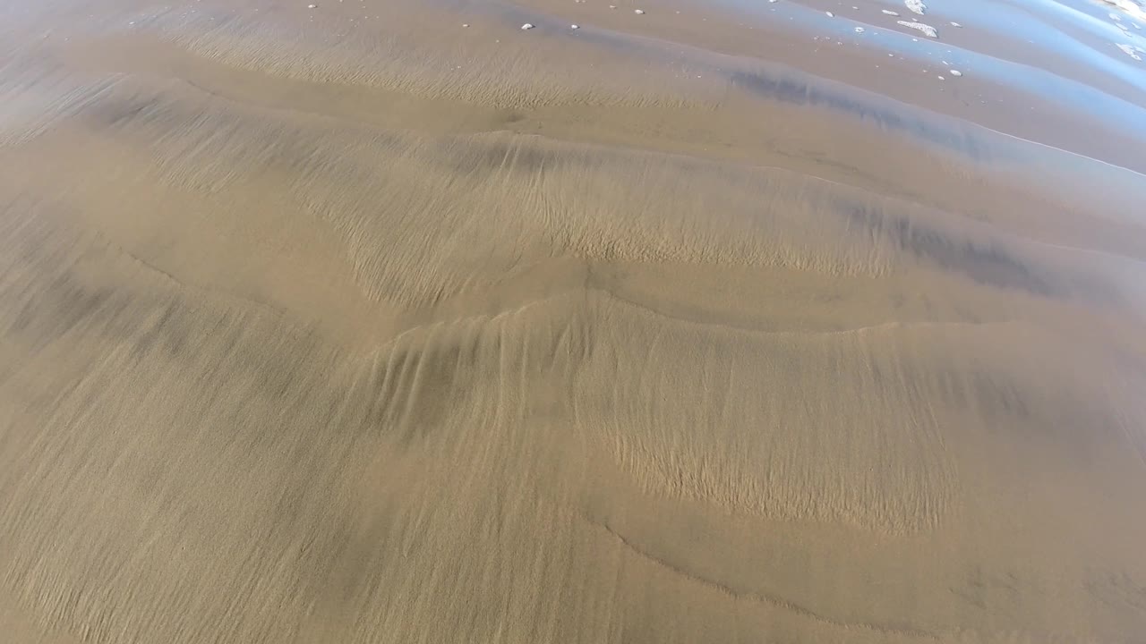 Curved damp lines and fine sand ridges run across the Pismo Beach shoreline, with shallow water at the top and no visible people.