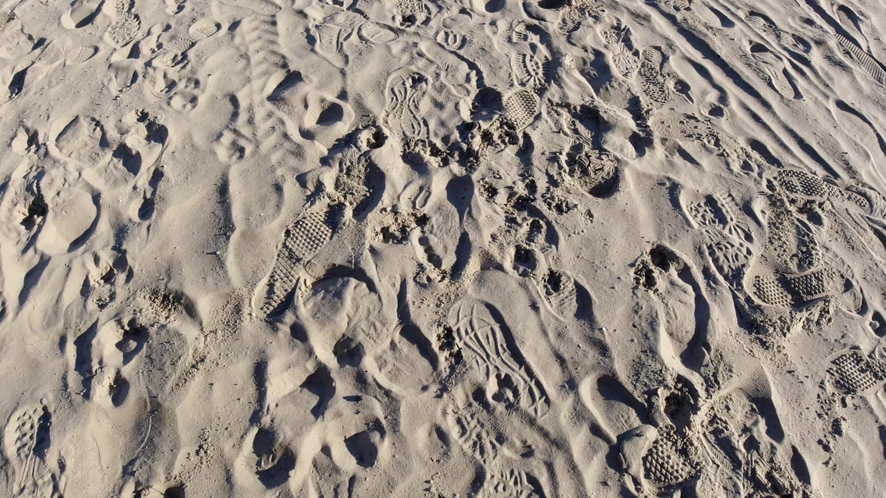 Overhead view of footprint-marked sand in Pismo Beach, California, with shoe treads, small pits, and no visible people.