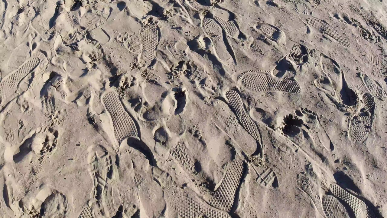 An overhead Pismo Beach sand detail shows crisscrossed tracks, deeper heel marks, textured shoe tread patches, and no visible people.