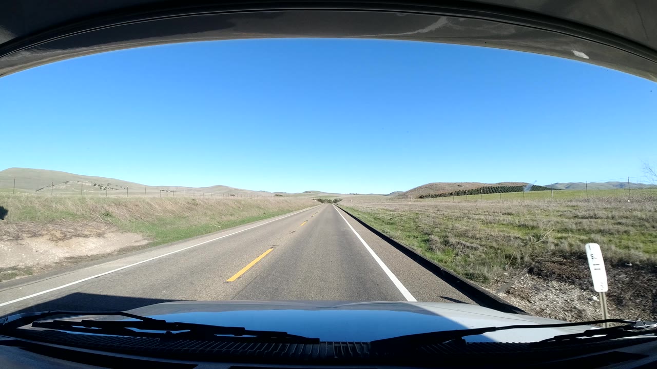 Straight rural road with grassy hills and windshield foreground.