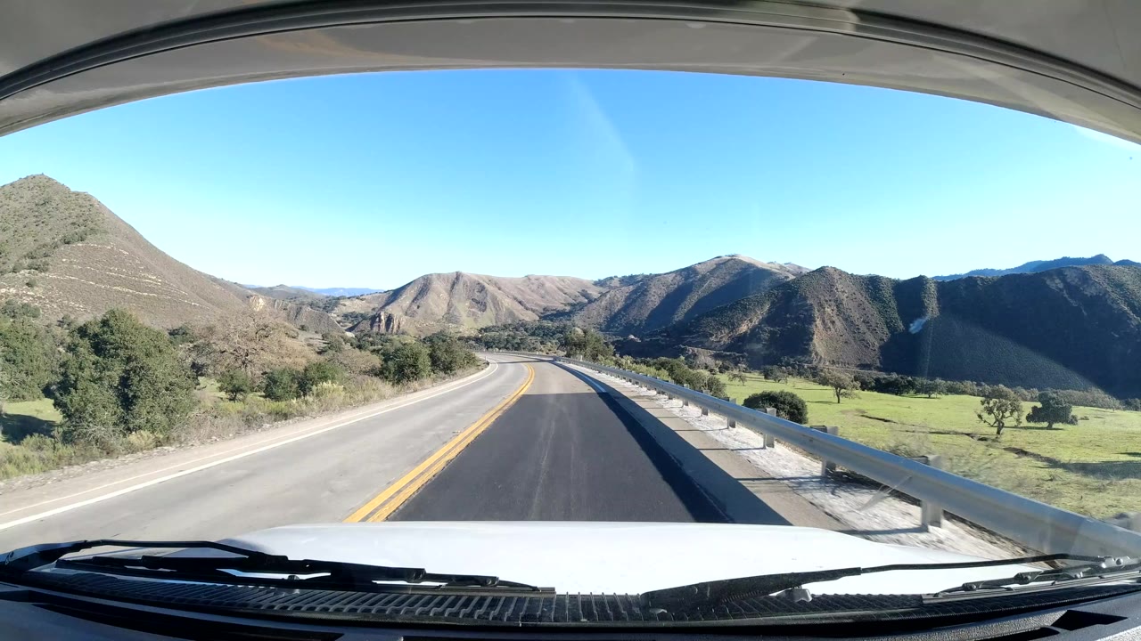 Two-lane road curving through hills from a vehicle windshield view.