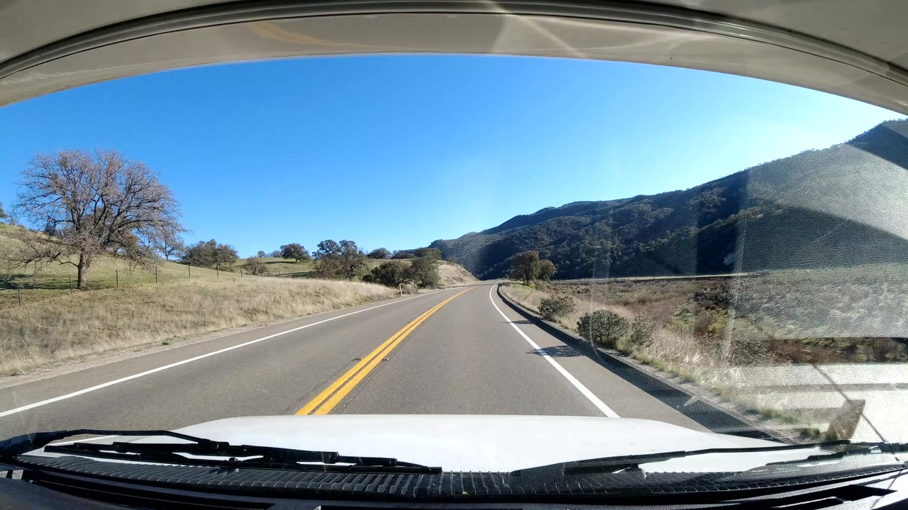 Roadside fields, bare trees, and mountains seen through a windshield.