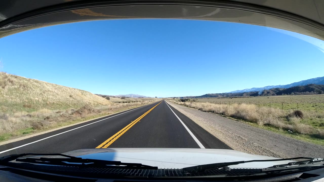 Empty two-lane road running between pale grass hills and a gravel shoulder.