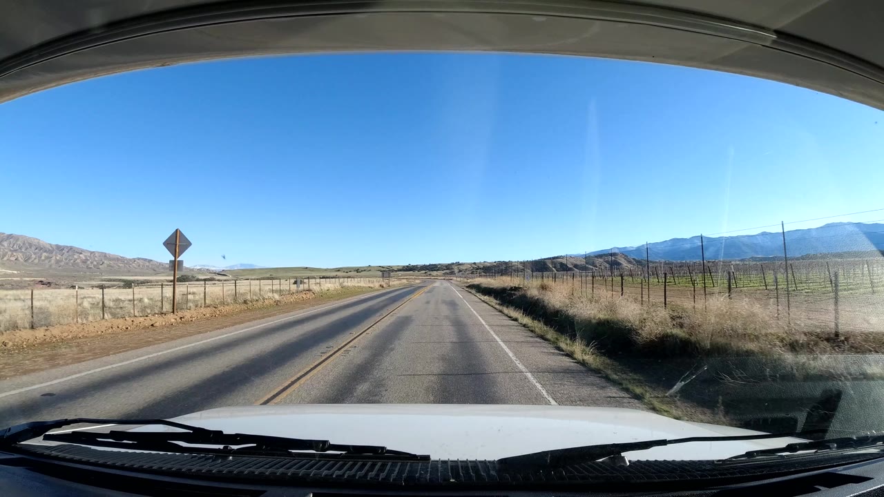 Country road with a diamond warning sign, fence, fields, and mountains in the distance.