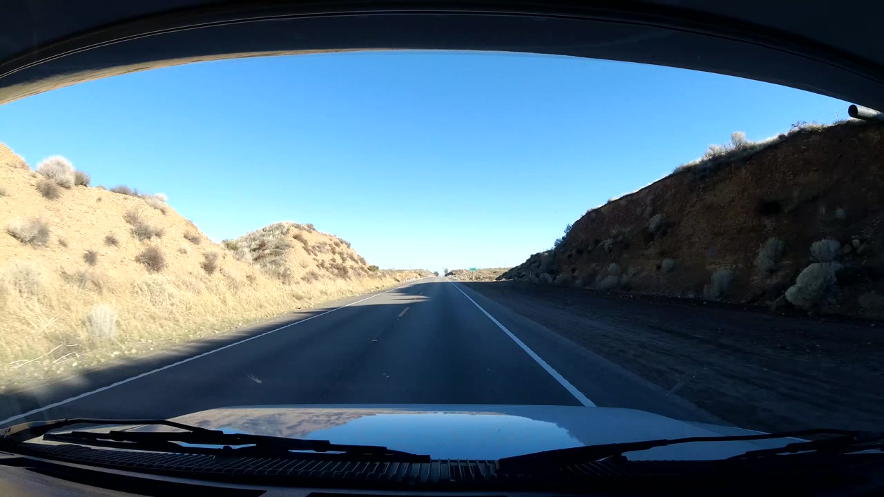Dash view of road curving through dry hillside terrain.