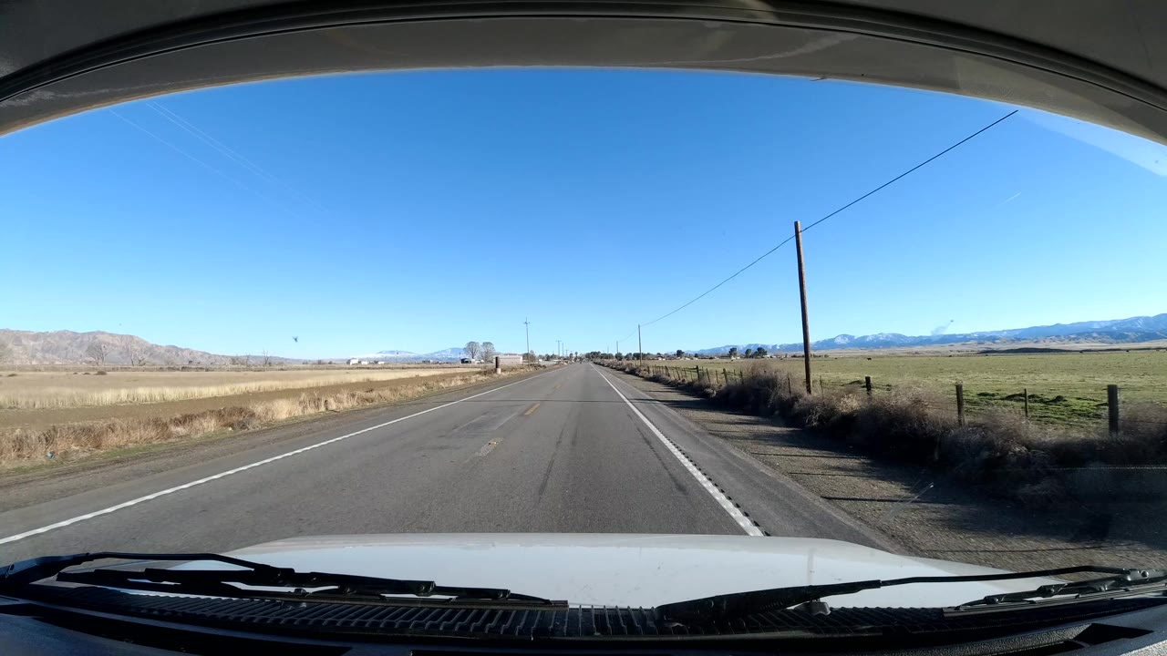 Dashboard view in Central Coast California looking down a straight two-lane road bordered by dry fields and distant mountains, with no visible people.