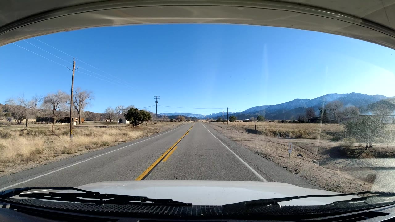 Two-lane rural road leading toward distant mountains under blue sky.