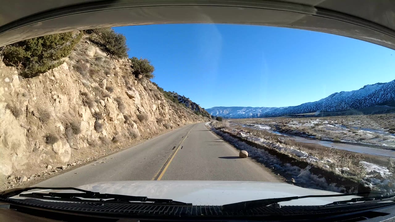 Road edge beside a cut hillside with snowy valley and mountains to the right.