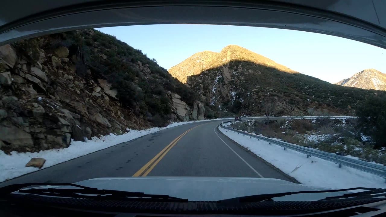 Road bending left beside a rock wall and snow-covered shoulder.