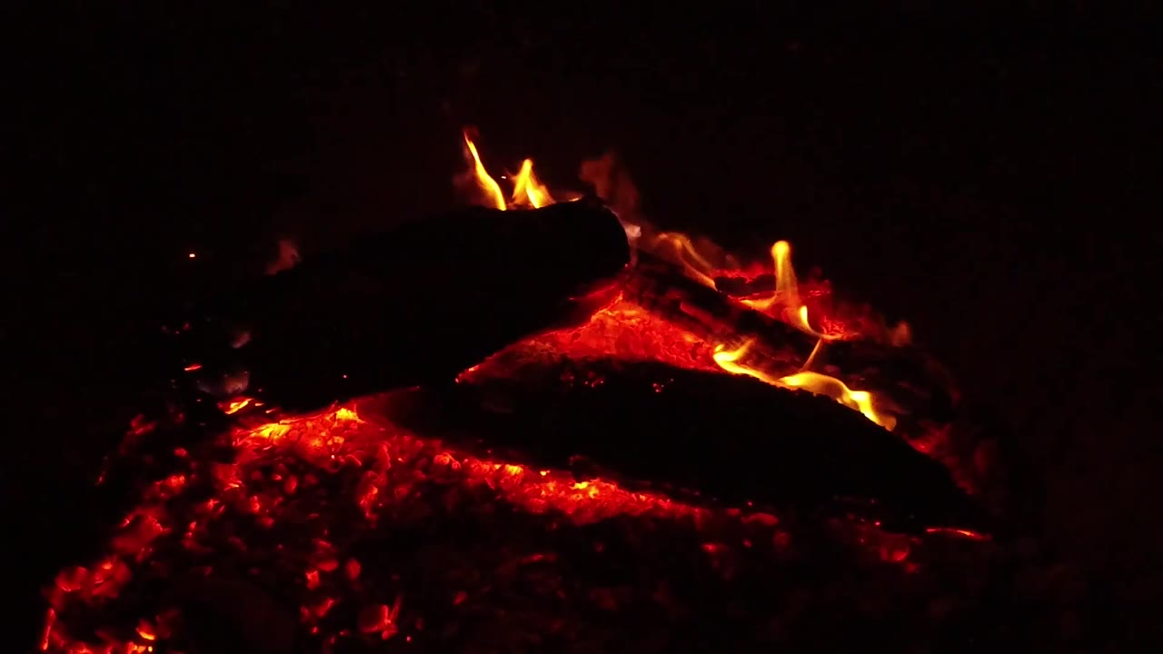 Small orange flames curl above a dark log while red coals glow below in Ojai, California, with no visible people.