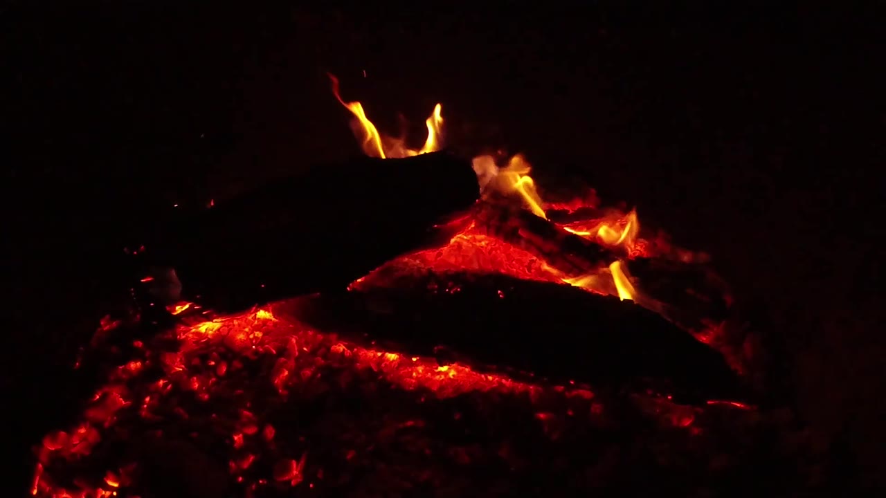 A brighter flame rises between two charred pieces of wood over red embers in Ojai, California, with no visible people.